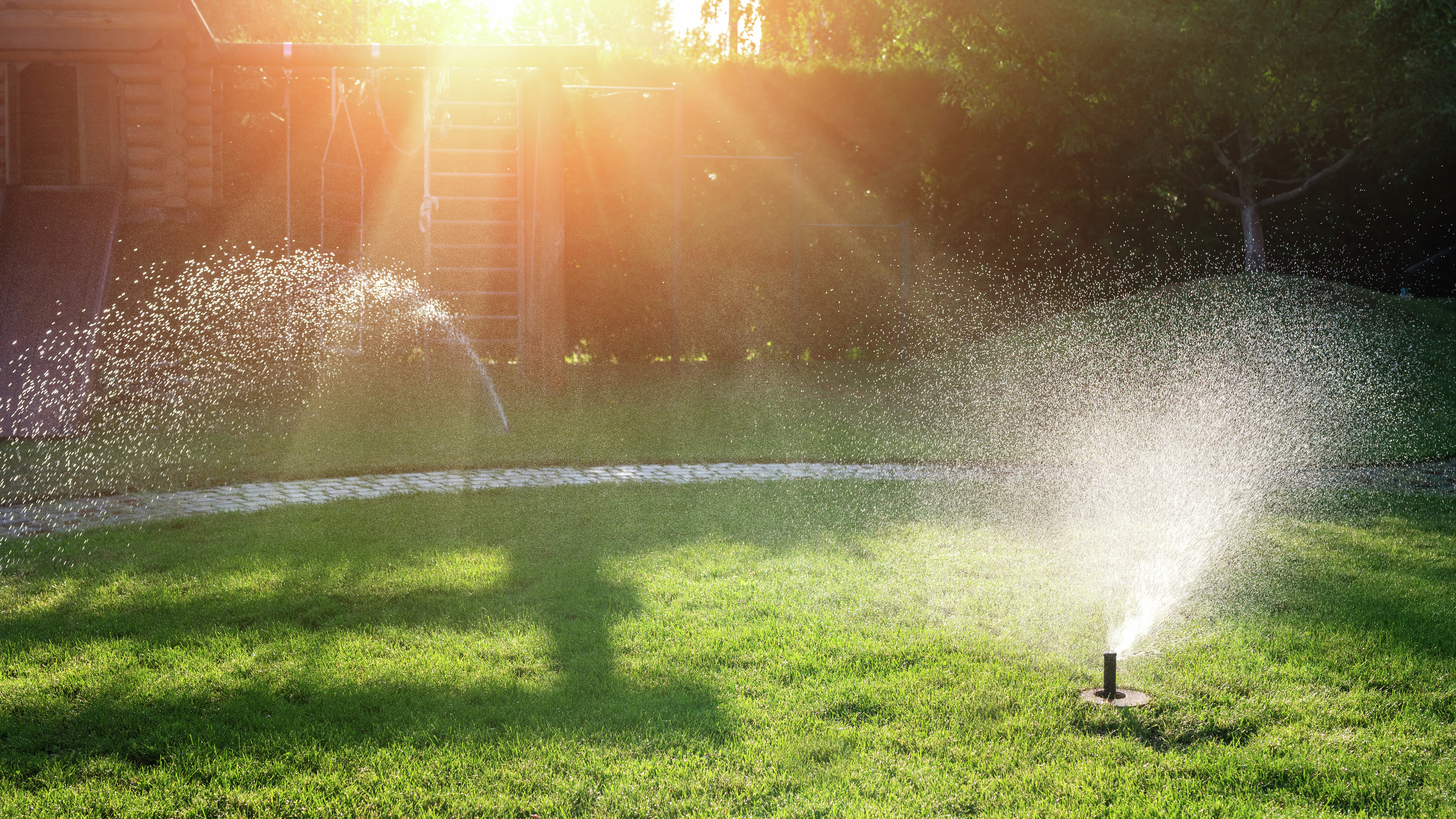 Sprinkler system watering green grass with sun shining down on the lawn
