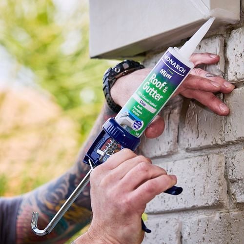 Hands using caulking gun to apply roof and gutter sealant to gutter.