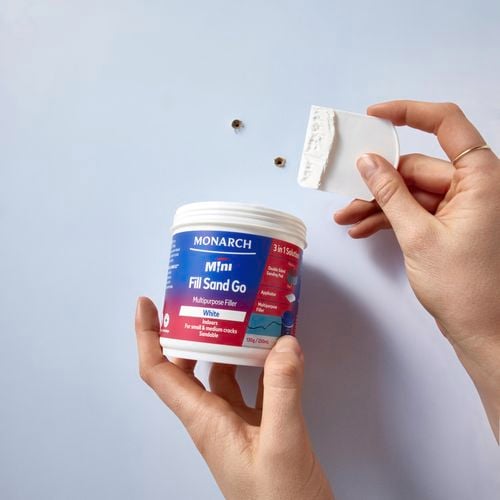 Hands holding fill sand go and applicator to apply to two holes in the wall.