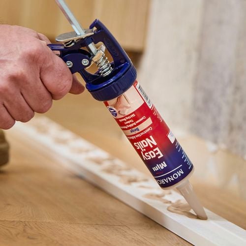 Hand holding a caulking gun applying easy nails to piece of wood.