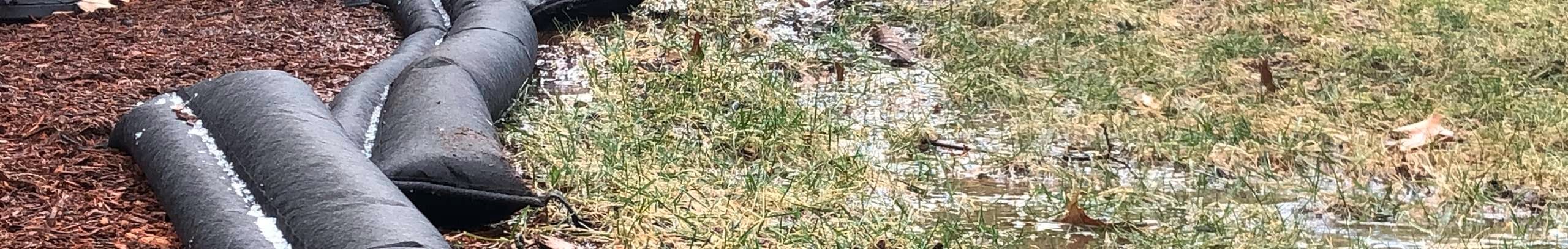 Flood barrier on ground in between grass and bark.